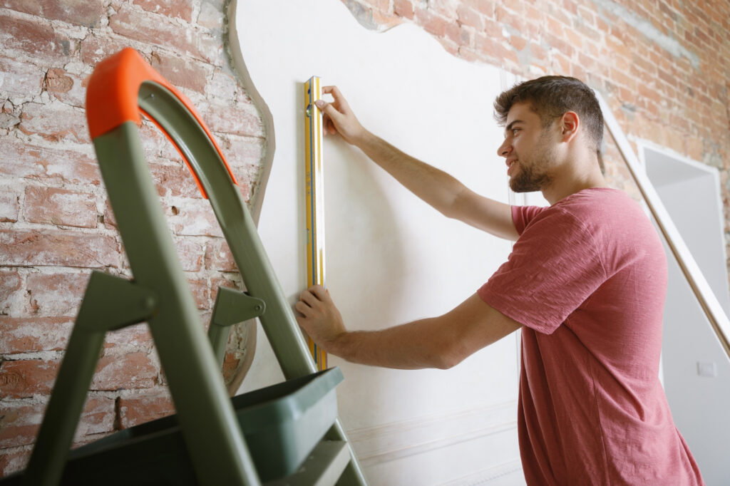 Young-man-preparing-doing-apartment-repair-by-hisselfes-before-home-makeover-renovation-concept-relations-family-diy-measuring-wall-before-painting-design-making